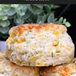 Freshly baked cheddar dill biscuits brushed with garlic dill butter stacked on a black plate.
