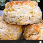 Freshly baked cheddar dill biscuits brushed with garlic dill butter stacked on a black plate.