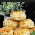 Freshly baked cheddar dill biscuits brushed with garlic dill butter stacked on a black plate.