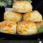 Freshly baked cheddar dill biscuits brushed with garlic dill butter stacked on a black plate.