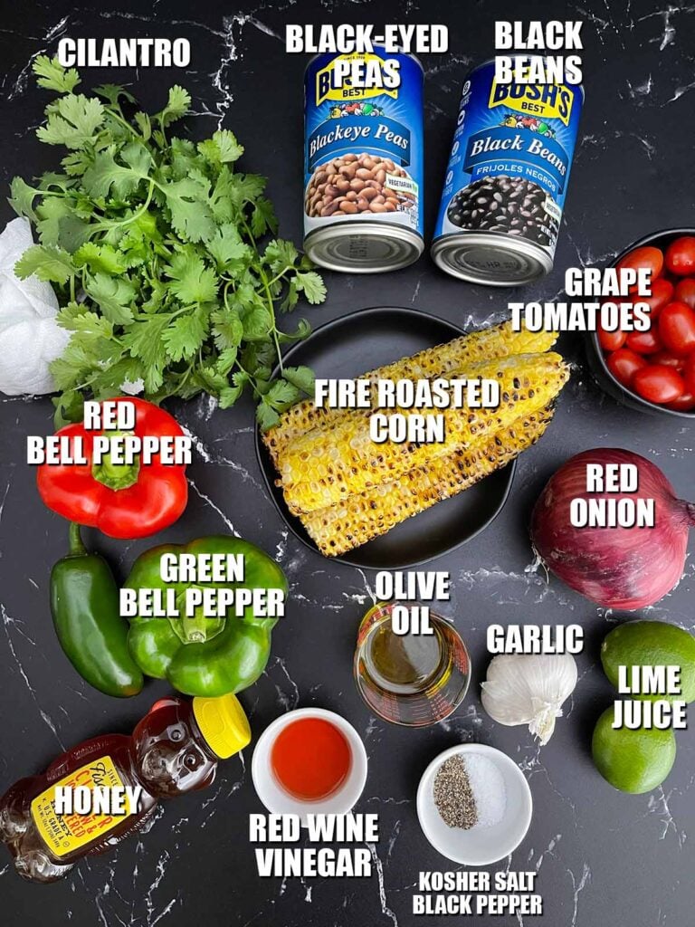 Ingredients for Cowboy Caviar including black beans, black-eyed peas, fire-roasted corn, bell peppers, tomatoes, red onion, jalapeño, cilantro, olive oil, lime, vinegar, honey, garlic, salt, and pepper.