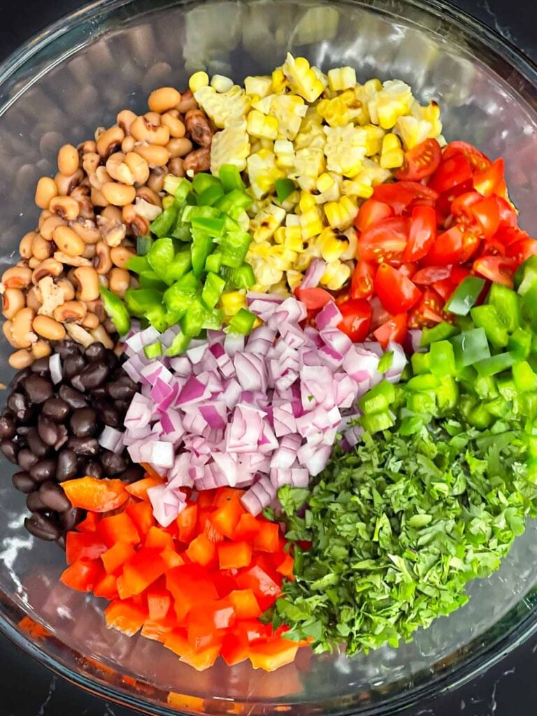Black beans, black-eyed peas,fire-roasted corn, bell peppers, jalapeno, tomatoes, red onion, and cilantro added to a large mixing bowl.