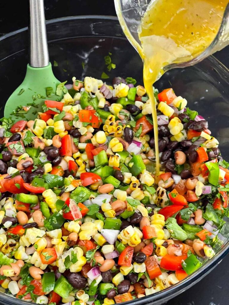 Homemade lime dressing being poured over Cowboy Caviar ingredients.