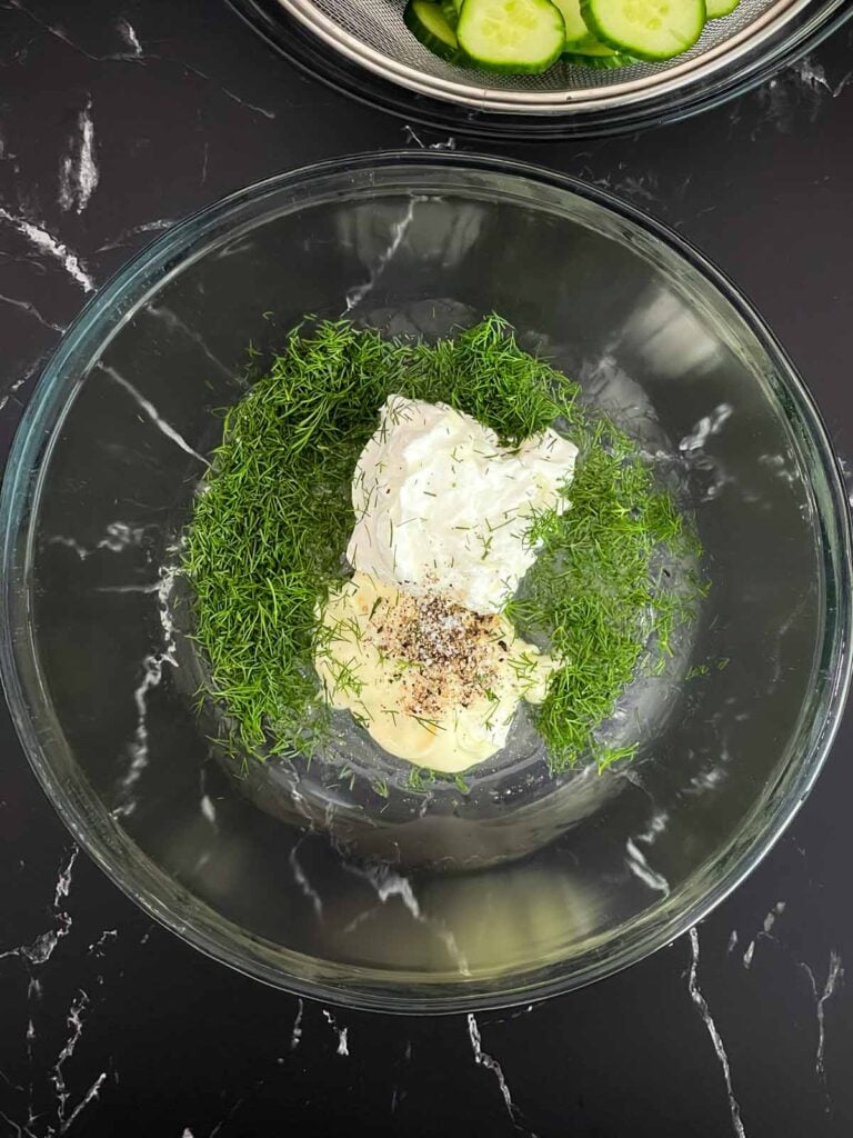 Sour cream, mayonnaise, white wine vinegar, fresh dill, salt, and pepper in a mixing bowl before whisking.