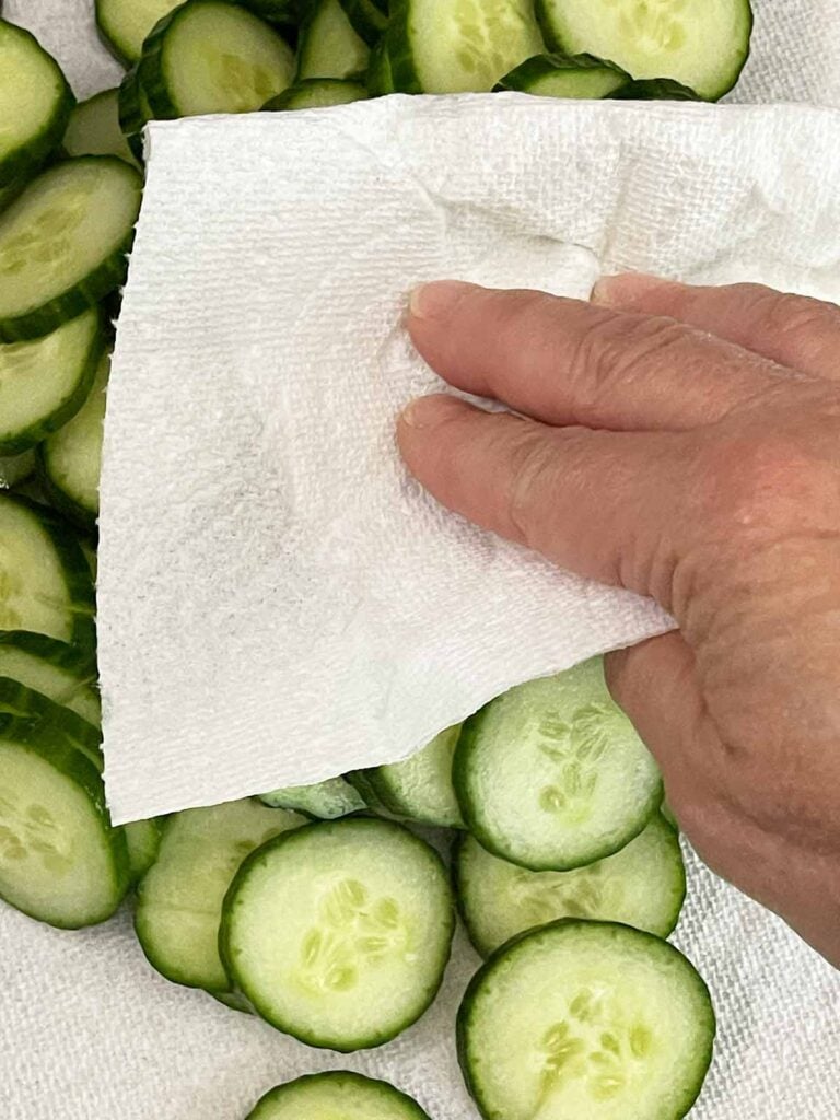 Patting sliced cucumbers dry to remove excess moisture before mixing into the salad.