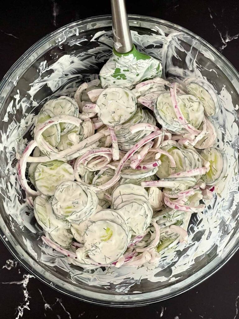 Tossing cucumbers and red onion in a creamy dill dressing until evenly coated.