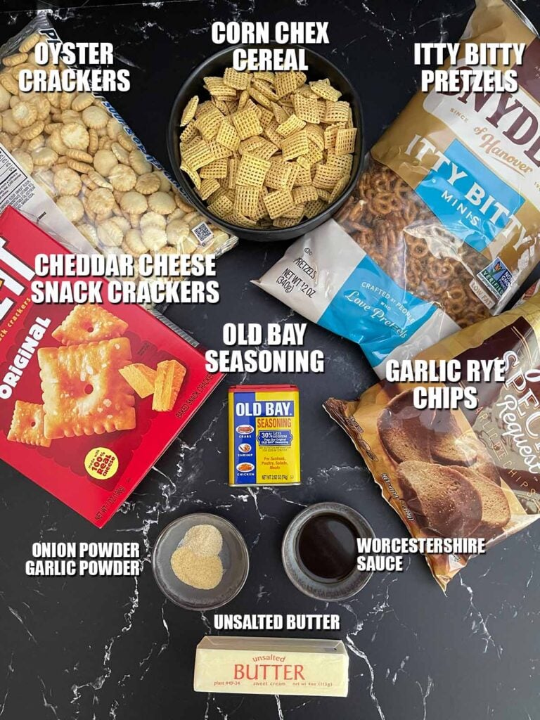 Ingredients for Old Bay Snack Mix including Corn Chex cereal, oyster crackers, pretzels, cheddar crackers, garlic rye chips, butter, Worcestershire sauce, Old Bay seasoning, garlic powder, and onion powder.