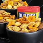 Old Bay Snack Mix served in a black bowl with Corn Chex cereal, pretzels, oyster crackers, cheddar crackers, and garlic rye chips.