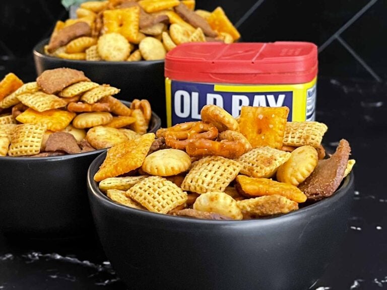Old Bay Snack Mix served in a black bowl with Corn Chex cereal, pretzels, oyster crackers, cheddar crackers, and garlic rye chips.
