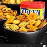 Homemade Old Bay Snack Mix served in a black bowl with Corn Chex cereal, pretzels, oyster crackers, cheddar crackers, and garlic rye chips.