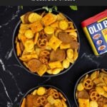 Easy Old Bay Snack Mix served in a black bowl with Corn Chex cereal, pretzels, oyster crackers, cheddar crackers, and garlic rye chips.