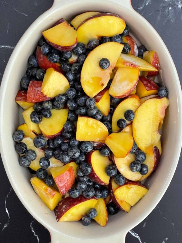Peach and blueberry filling spread into a buttered baking dish.