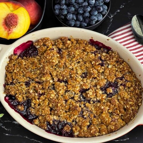 Freshly baked Easy Peach Blueberry Crisp in a white baking dish with a golden brown oat topping and bubbling peach and blueberry filling before serving.