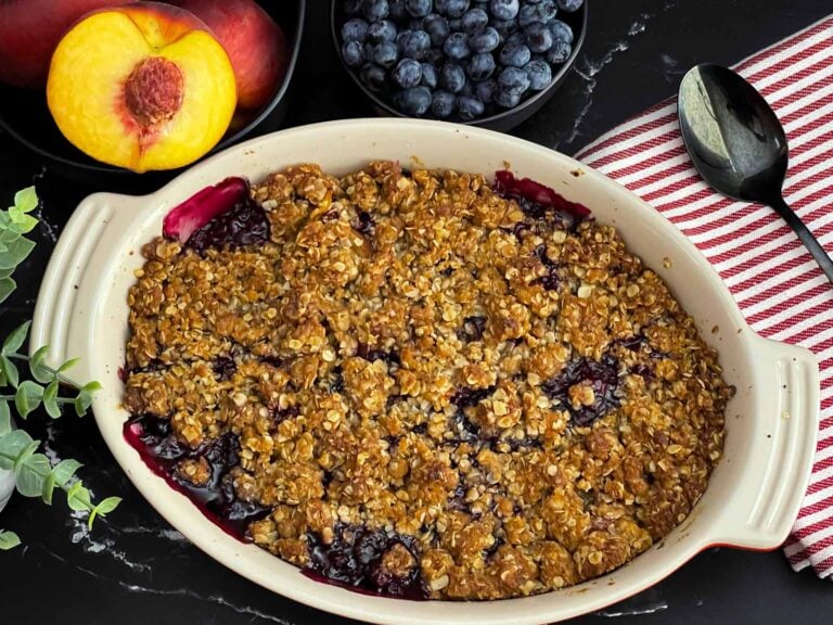Freshly baked Easy Peach Blueberry Crisp in a white baking dish with a golden brown oat topping and bubbling peach and blueberry filling before serving.