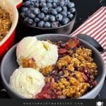 Golden brown Easy Peach Blueberry Crisp with a buttery oat topping served warm in a grey bowl with a scoop of vanilla ice cream melting over the fruit.