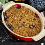 Freshly baked Easy Peach Blueberry Crisp in a red baking dish with a golden brown oat topping and bubbling peach and blueberry filling before serving.