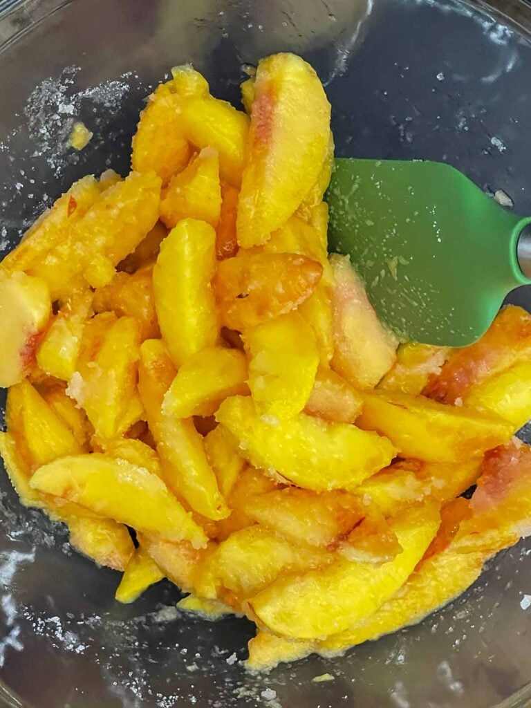 Fresh peach slices tossed with lemon juice and sugar in a mixing bowl.