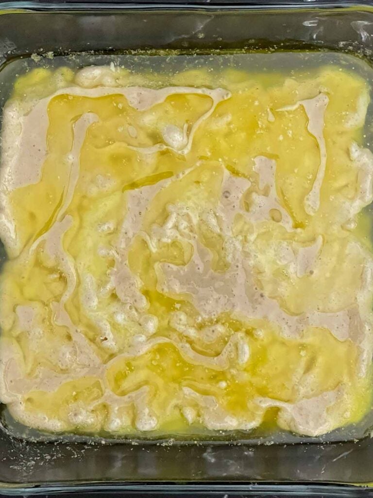 Peach cobbler batter poured over melted butter in a baking dish without stirring.