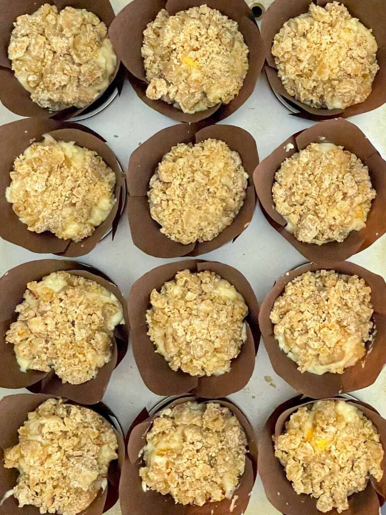 Unbaked peach muffins topped generously with cinnamon streusel before baking.