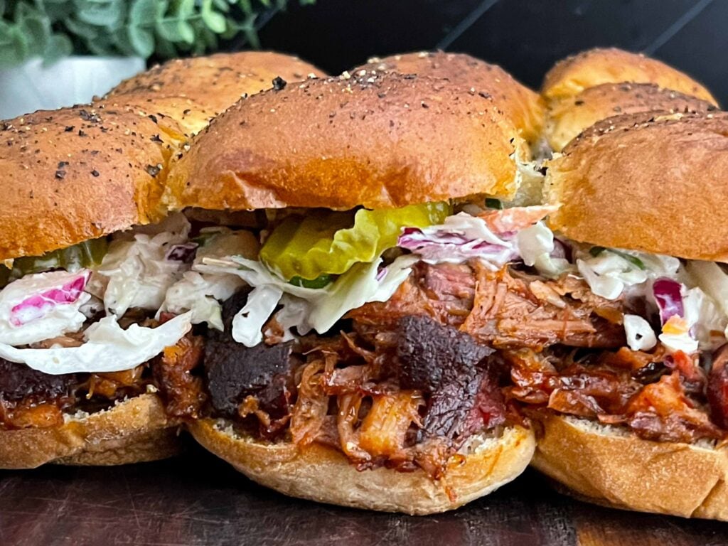 Close-up of homemade pulled pork sliders with barbecue sauce, creamy coleslaw, and dill pickles.