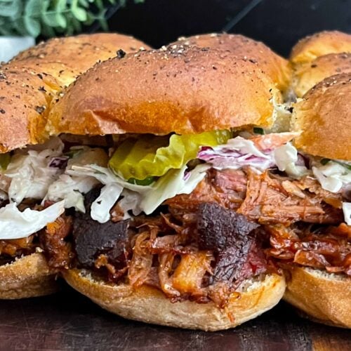 Close-up of homemade pulled pork sliders with barbecue sauce, creamy coleslaw, and dill pickles.