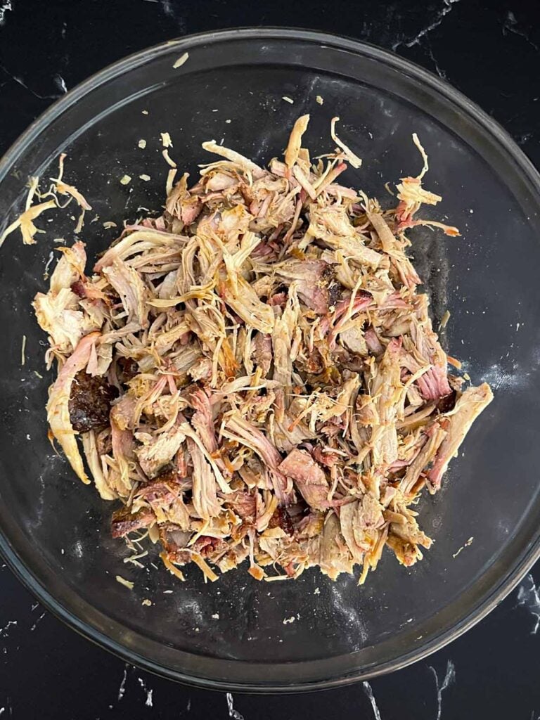 Chopped smoked pulled pork in a glass mixing bowl.