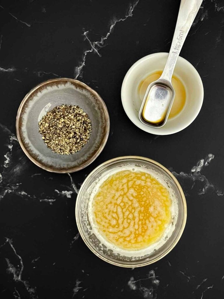 Melted butter mixed with Worcestershire sauce beside freshly cracked black pepper.