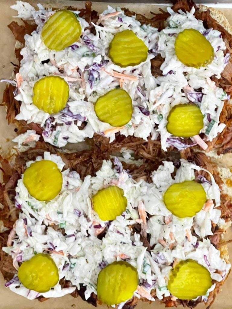 Creamy coleslaw and dill pickle chips added to pulled pork sliders after baking.