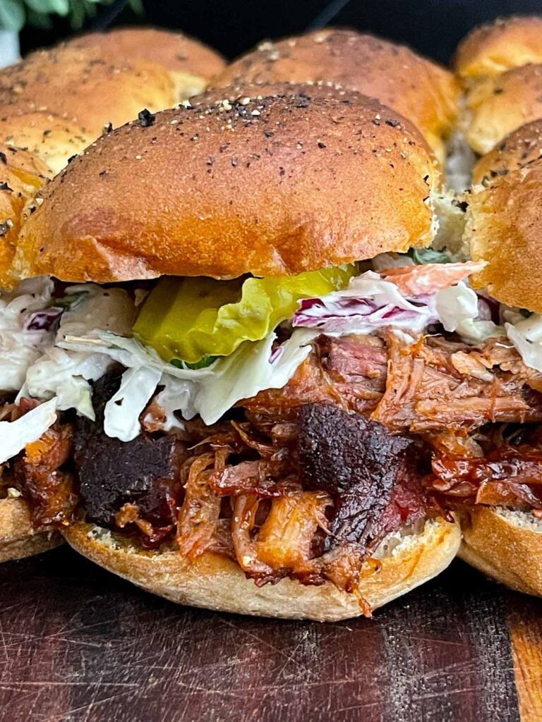 Finished pulled pork sliders assembled with coleslaw and dill pickles on savory rolls.