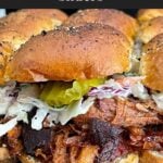 Finished pulled pork sliders assembled with coleslaw and dill pickles on savory rolls.