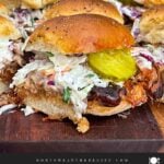 Finished pulled pork sliders assembled with coleslaw and dill pickles on savory rolls.