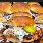 Finished pulled pork sliders assembled with coleslaw and dill pickles on savory rolls.