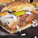 Finished pulled pork sliders assembled with coleslaw and dill pickles on savory rolls.