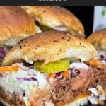 Finished pulled pork sliders assembled with coleslaw and dill pickles on savory rolls.