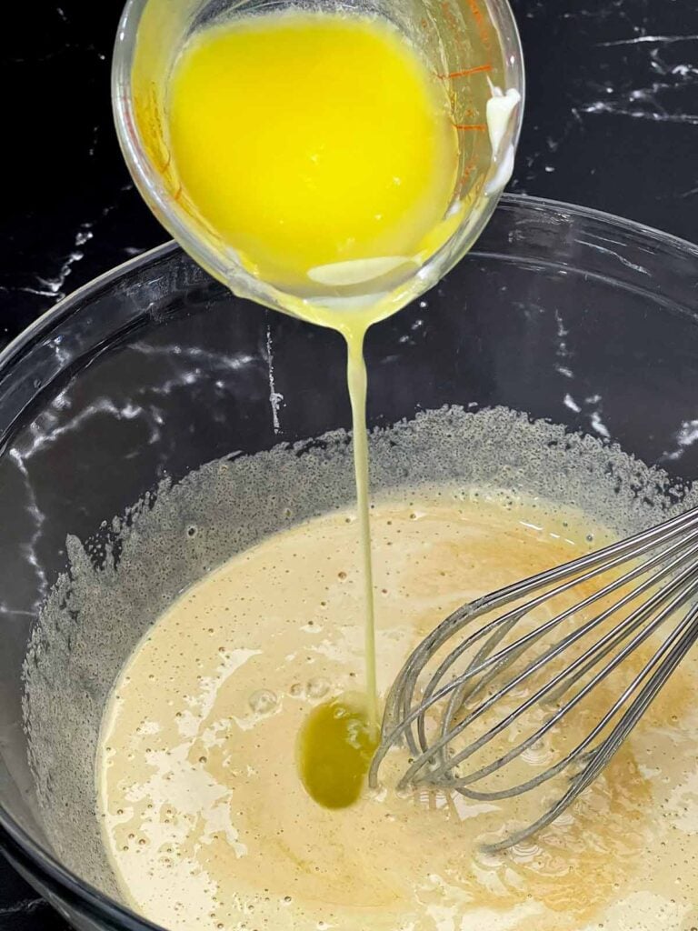 Melted butter and vanilla being whisked into the egg and sugar mixture.