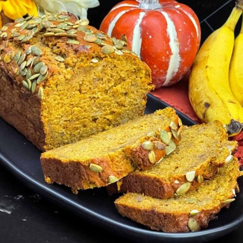 Sliced pumpkin banana bread topped with pumpkin seeds on a black platter.