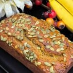 Freshly baked pumpkin banana bread topped with pumpkin seeds on a black platter.