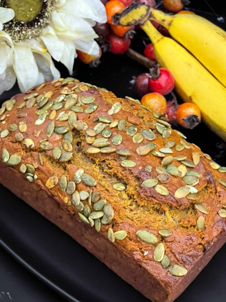 Freshly baked pumpkin banana bread topped with pumpkin seeds on a black platter.