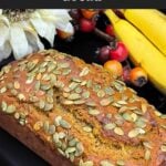 Freshly baked pumpkin banana bread topped with pumpkin seeds on a black platter.