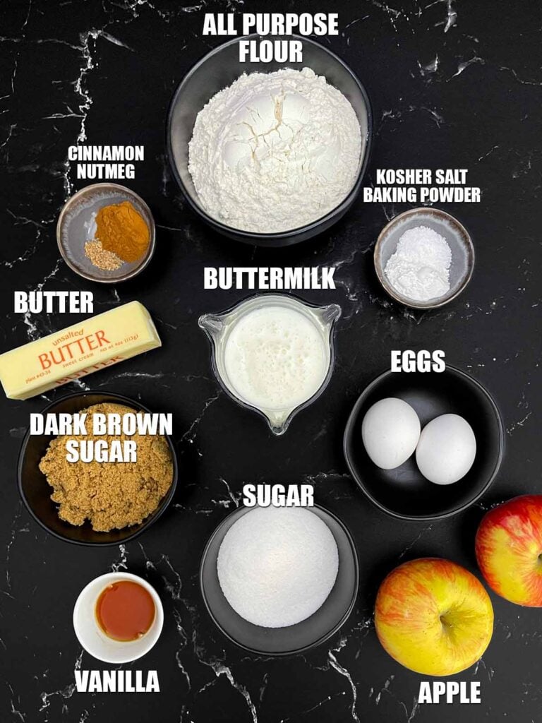 Ingredients for apple cinnamon muffins including fresh apples, flour, buttermilk, butter, eggs, sugars, cinnamon, nutmeg, and vanilla.