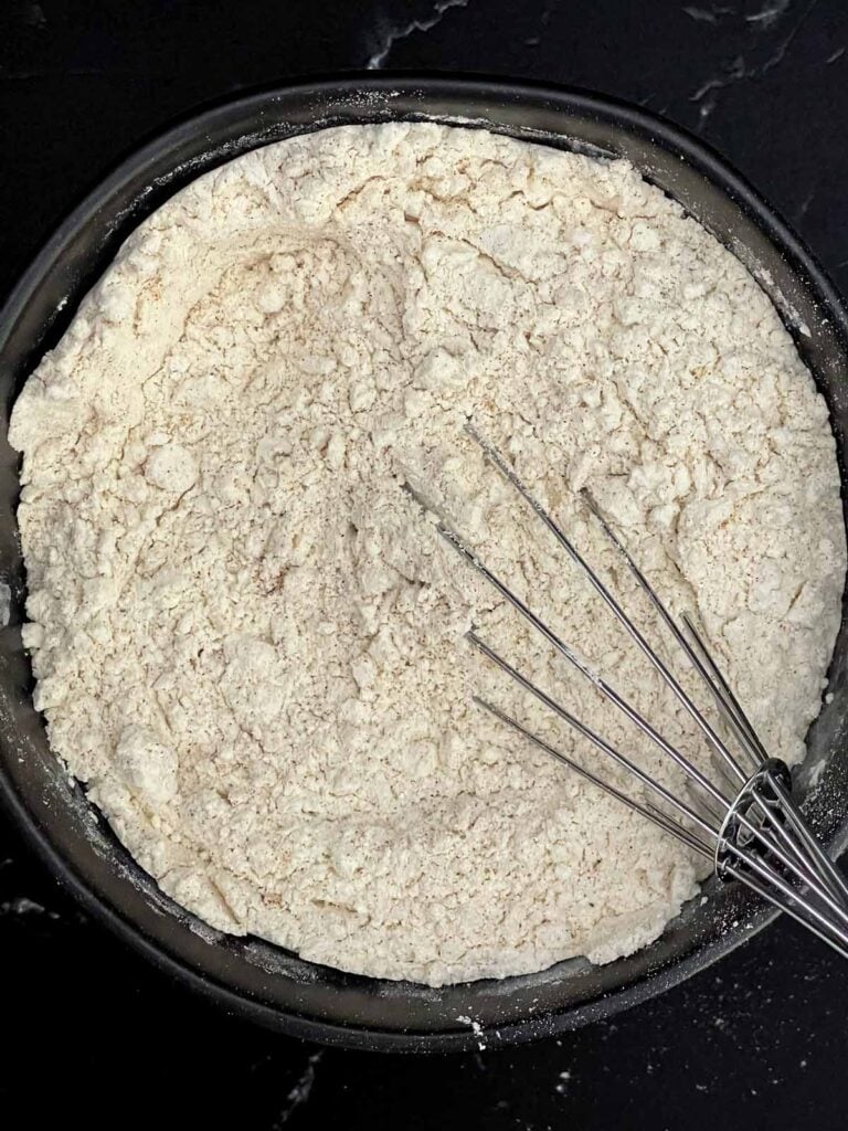 Flour, baking powder, cinnamon, nutmeg, and salt whisked together in a mixing bowl.