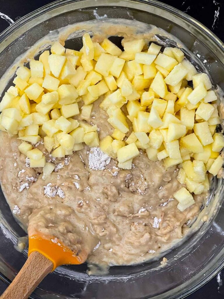 Diced apples added to the thick cinnamon muffin batter in a mixing bowl.