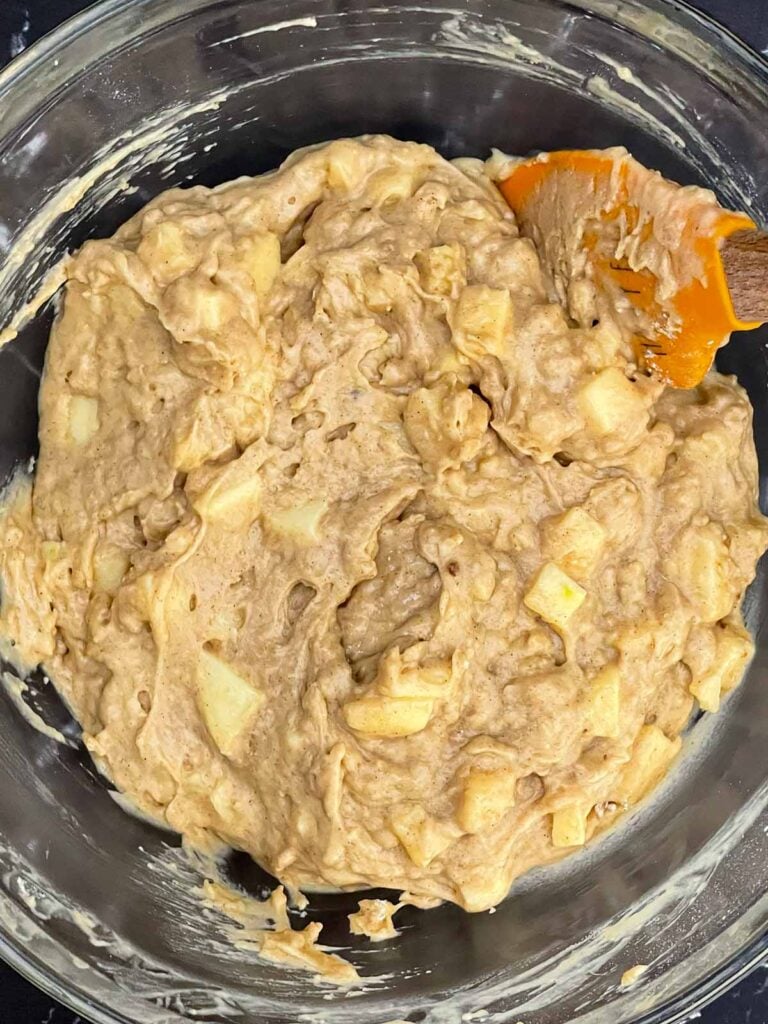 Diced apples folded into thick cinnamon muffin batter in a mixing bowl.