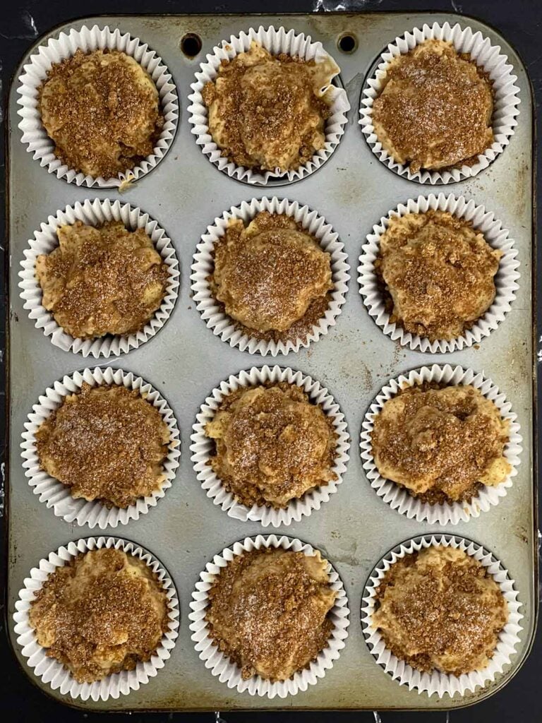 Apple cinnamon muffin batter portioned into a lined muffin pan and topped with cinnamon sugar.