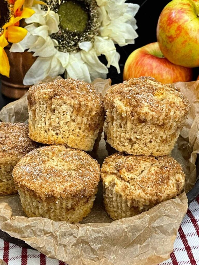 Apple cinnamon muffins with cinnamon sugar tops stacked in a cake pan lined with parchment paper.