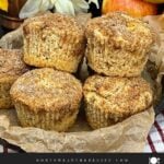 Bakery-style apple cinnamon muffins with cinnamon sugar tops stacked in a cake pan lined with parchment paper.