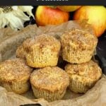Bakery-style apple cinnamon muffins with cinnamon sugar tops stacked in a cake pan lined with parchment paper.