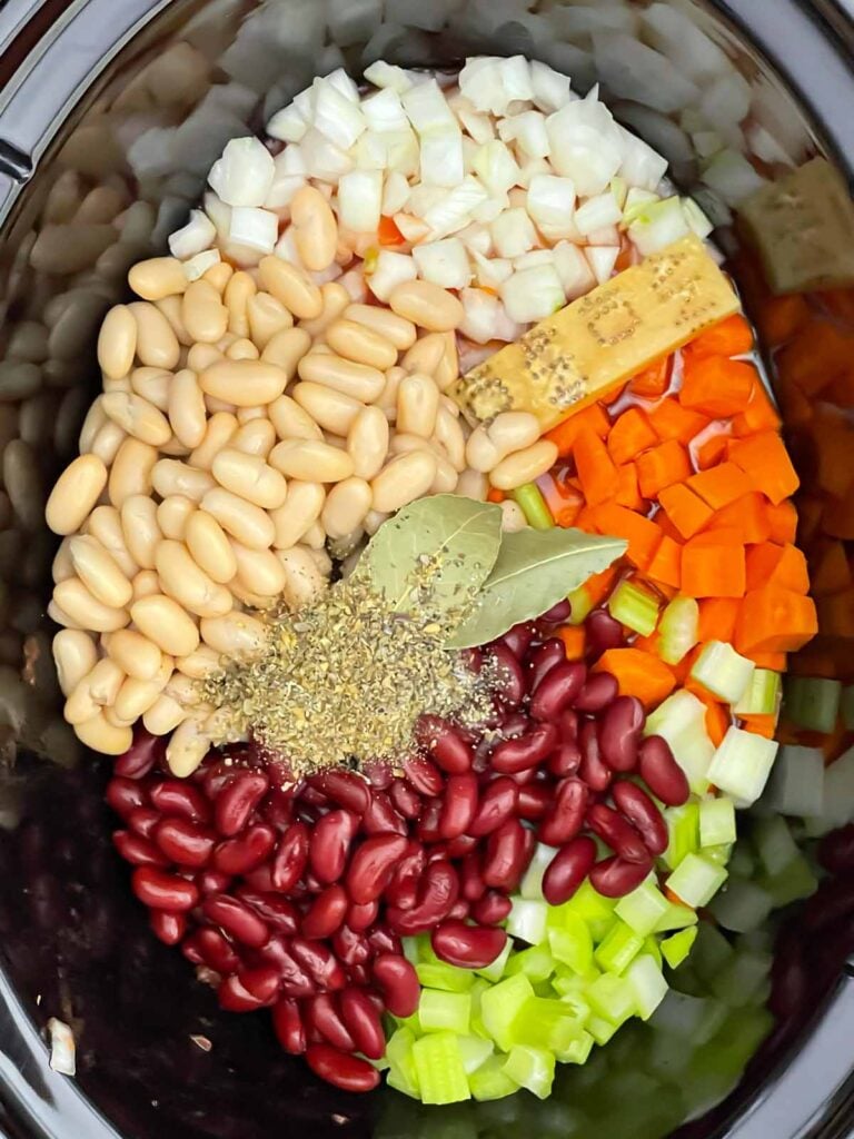 Vegetable stock, tomatoes, beans, carrots, celery, onion, garlic, Parmesan rind and seasonings in a slow cooker.