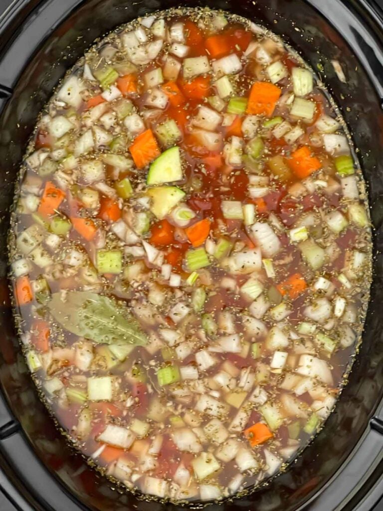 Vegetable stock, tomatoes, beans, carrots, celery, onion, garlic, and seasonings stirred together in a slow cooker crock.