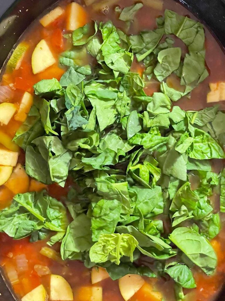 Fresh spinach in the slow cooker minestrone soup with vegetables and beans.